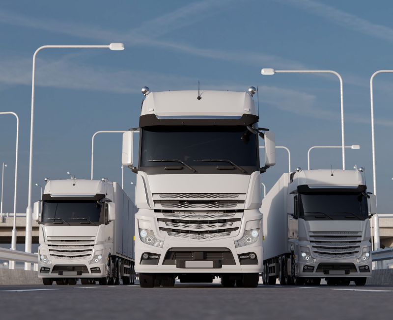 A row of modern white trucks parked under streetlights against a clear blue sky.